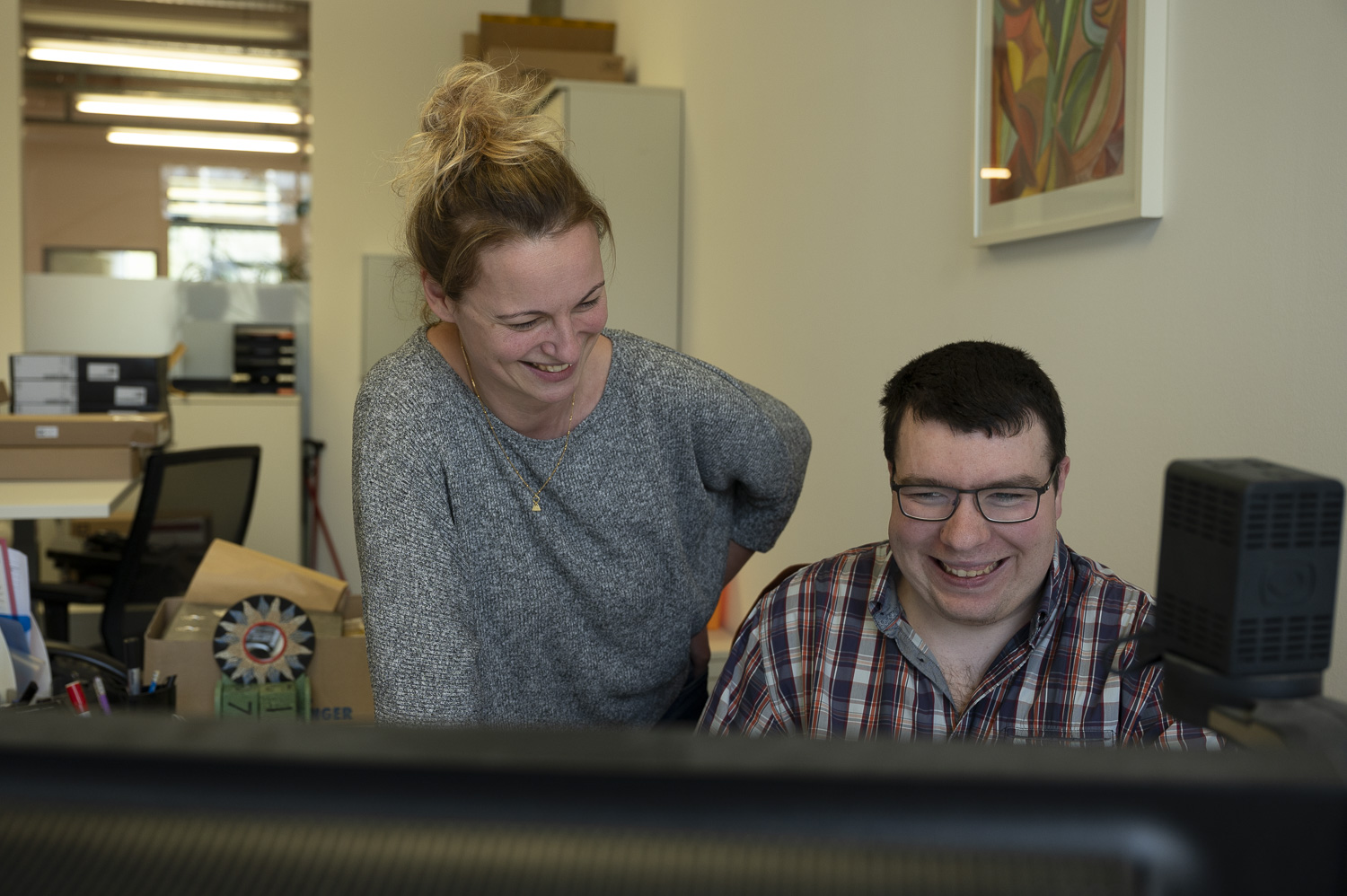 Eine Mitarbeiterin der diakonia schaut einem Mann an einem Desktop über die Schulter.